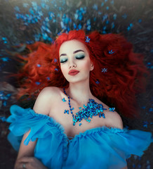 Butterfly girl in a necklace of blue butterflies lies in the forest in flowers. Female fairy in a...
