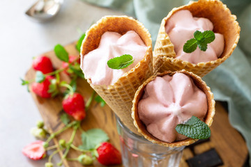 Homemade Organic Strawberry Ice Cream. Strawberry of ice cream in waffle cones on a light stone or slate table. Top view flat lay background.