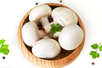 A bunch of fresh porcini mushrooms in a wooden bowl on a white background with parsley, pepper and Bay leaf.