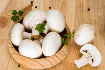 A bunch of fresh porcini mushrooms in a wooden bowl on a wooden background with parsley and pepper.