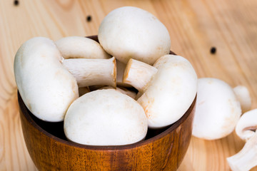 A bunch of fresh porcini mushrooms in a wooden bowl on a wooden background with parsley and pepper.