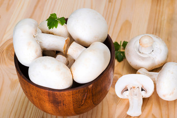 A bunch of fresh porcini mushrooms in a wooden bowl on a wooden background with parsley and pepper.