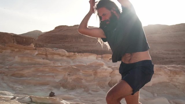 Handsome man practice ecstatic dance in desert in sunshine rapid slow motion