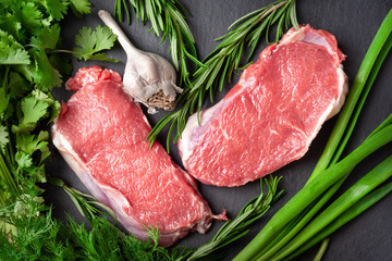Raw meat. Top view of two slices of fresh raw meat, a branch of rosemary and garlic on a black slate stone board. Preparing meat for a barbecue.