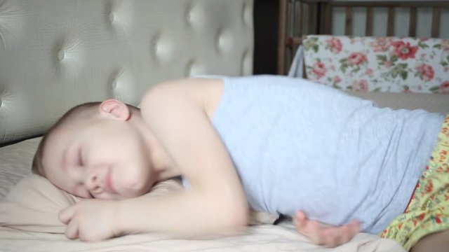 Blonde boy sleeping in a bed in his bedroom and tossing and turning.
