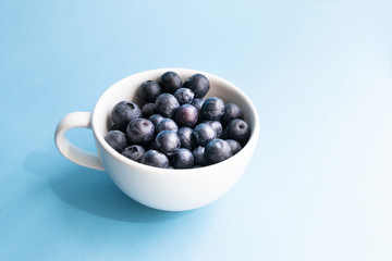 Fresh raw organic blueberry in a mug on blue surface