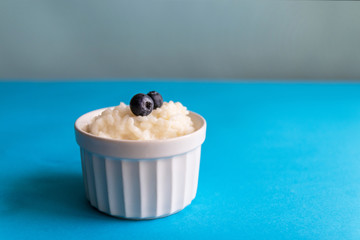 Tasty rice porridge in a white bowl on a blue background with copy space. Proper healthy eating breakfast concept.