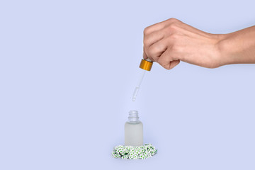 female hand holds a dropper from a bottle with oil. Glass container for a cosmetic product for women with small white flowers on a lilac background