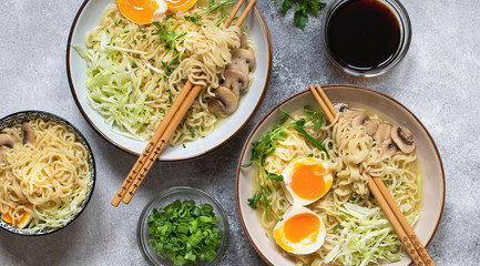 Asian ramen noodle soup with mushrooms, cabbage, green onions and egg. Japanese street food. Gray background, flat lay, copy space