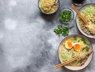 Asian ramen noodle soup with mushrooms, cabbage, green onions and egg. Japanese street food. Gray background, flat lay, copy space