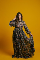 Happy girl in a long dress on yellow background with a bouquet of flowers