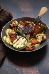 Grilled vegetables (zucchini, cherry tomatoes, onions, champignons, bell peppers) served in a plate with rosemary and sea salt on a dark vintage background. Close-up. Copy space. Vertical