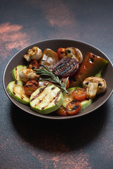 Grilled vegetables (zucchini, cherry tomatoes, onions, champignons, bell peppers) served in a plate with rosemary and sea salt on a dark vintage background. Close-up. Copy space. Vertical
