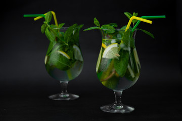Summer mint lime refreshing cocktail mojito with rum and ice in glass on black background. Mojito cocktail on dark stone table. Glassy high glass for drinks. Lemonade at the bar.