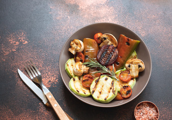 Grilled vegetables (zucchini, cherry tomatoes, onions, champignons, bell peppers) served in a plate with rosemary and sea salt on a dark vintage background. Top view. Copy space