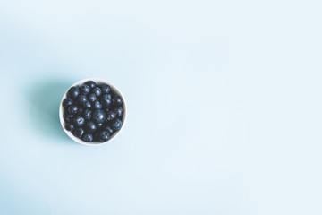 Ripe blueberry in cup with copyspace on blue background, top view, flat lay