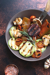 Grilled vegetables (zucchini, cherry tomatoes, onions, champignons, bell peppers) served in a plate with rosemary and sea salt on a dark vintage background. Top view. Copy space. Vertical