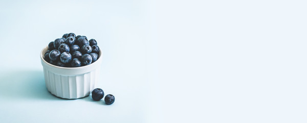 Fresh raw organic blueberry in a mug on a blue surface with copyspace