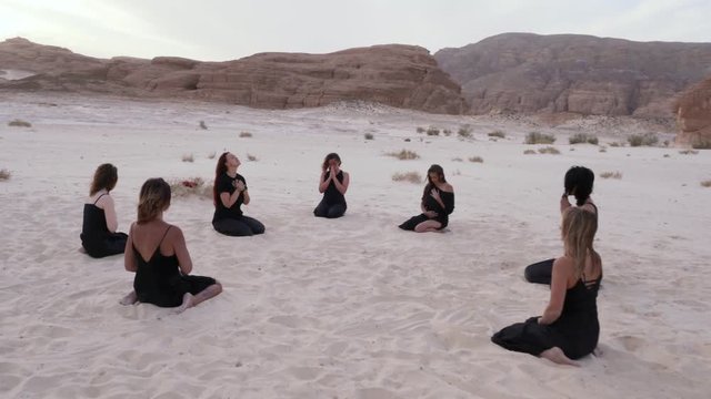 Group of women sitting in circle practicing meditation at sandy desert