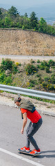 Male caucasian longboarder riding downhill on an empty road doing a speed tuck and grabbing the board while driving the longboard fast. Wearing a red t-shirt green hat and black jeans.