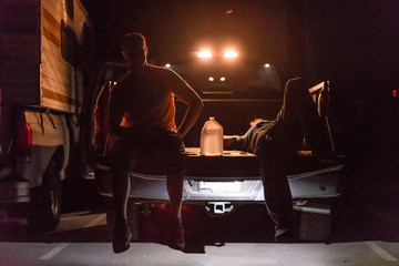 two men resting sitting back of truck backlit in the night water jug