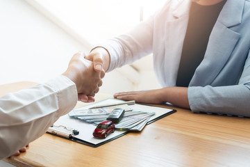 Car sales agent and client shaking hand after finishing signed the car rental agreement in the office.