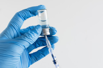 Doctor's hands in a blue gloves holding syringe and vaccine.