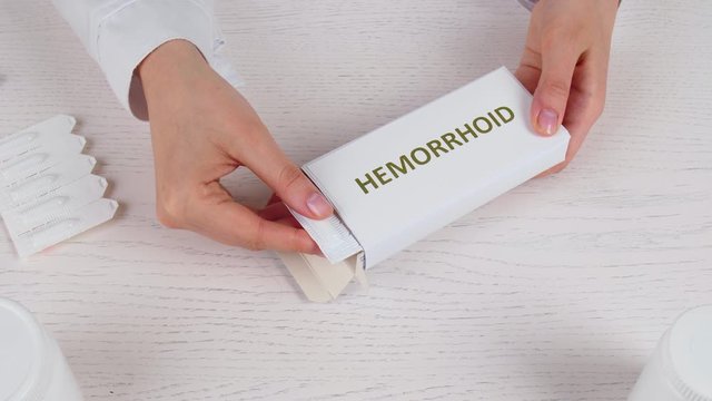 Proctologist with pack of hemorrhoidal suppositories at table