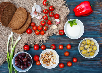 Some red fresh cherries, spring onions, coriander, cheese, garlic, olives in a bowl, bread on dark rustic wooden background. Flat Lay with no people. View from the top.