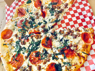 Gourmet pizza with pepperoni, sausage, and spinach in a traditional delivery box