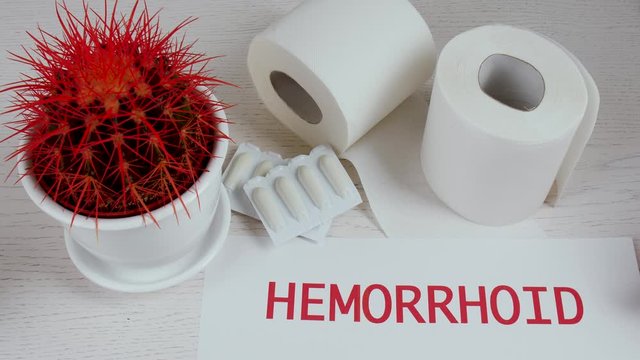 Putting of paper with word HEMORRHOID on table with cactus, suppositories and toilet paper