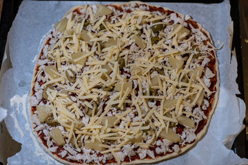 Raw pizza with pineapple, olives, chicken and cheese