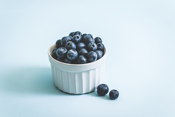 Fresh raw organic blueberry in mug on a blue surface with copy space