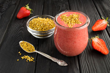 Smoothies with strawberry  and  bee pollen in the small glass jar on the black wooden background. Closeup.