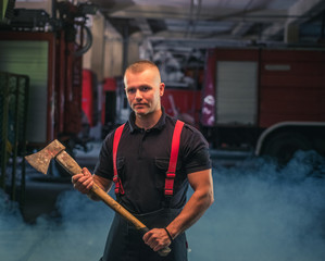 Fototapeta na wymiar Portrait of young firefighter holding an axe in the garage of the fire department.