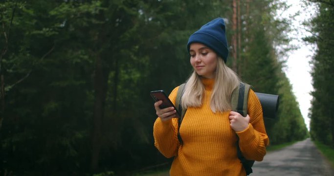 Girl with Backpack Using Smartphone Gps. Woman Hiking In The Forest And Typing Message On Smartphone. Solo female hiker using smart phone. Female hiker takes smart phone pic of mountains and forest.