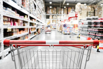 The empty red shopping cart in supermarket with blurred background.