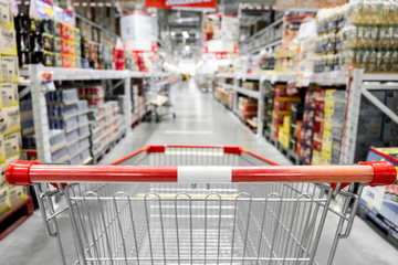 The empty red shopping cart in supermarket with blurred background.