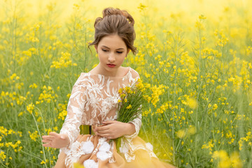 Portrait of Beautiful young girl in a dress picking rapeseed flowers in a field on a sunny day