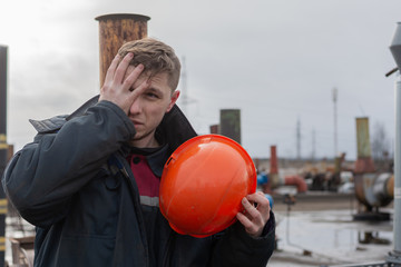 Worker builder stands on the roof of the factory. in one hand grips a helmet. the other hand covers...