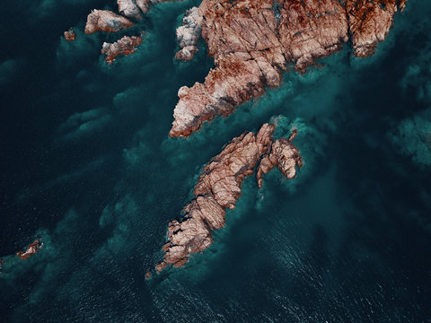 Aerial view of a reddish secluded reef diving in a transparent blue sea near Isola Rossa, Sardinia, Italy.