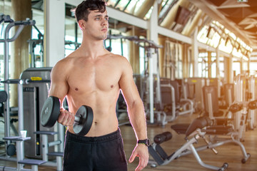Fototapeta na wymiar Young man lifting dumbbell and working out on his biceps at gym.