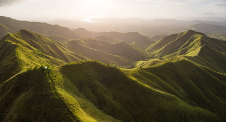 Panoramic aerial view of lush mountain ridge in the golden light of sunrise with the sea in the background. Labawan Peak, Bohol, Philippines