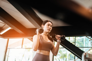 Young beautiful slim woman doing exercises with dumbbell in gym