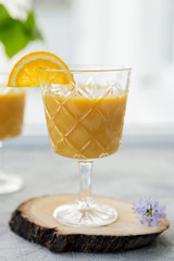 Smoothie with slice of orange as garnish on glass at gray background.