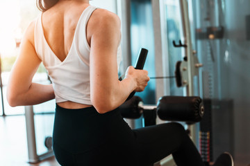 Fototapeta premium Close up back of young woman in sportswear working out with machine in gym