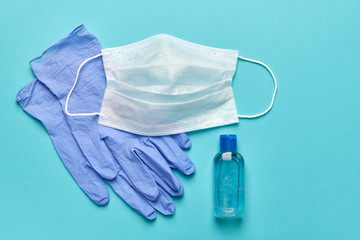 Medical mask, gloves and a bottle of antiseptics on a turquoise background, copy space.