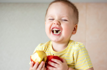 The boy is sitting on the kitchen table eating an Apple and laughing very hard