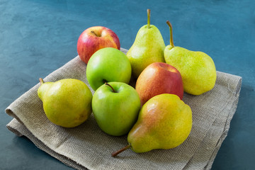 A few fresh bright apples and pears lie on a simple coarse rustic napkin on a blue background. Healthy eating. Horizontal orientation, selective focus. 