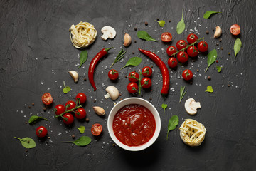 Tomato sauce and ingredients for its preparation, such as cherry tomatoes, red pepper, garlic, mushrooms and spices on a black background